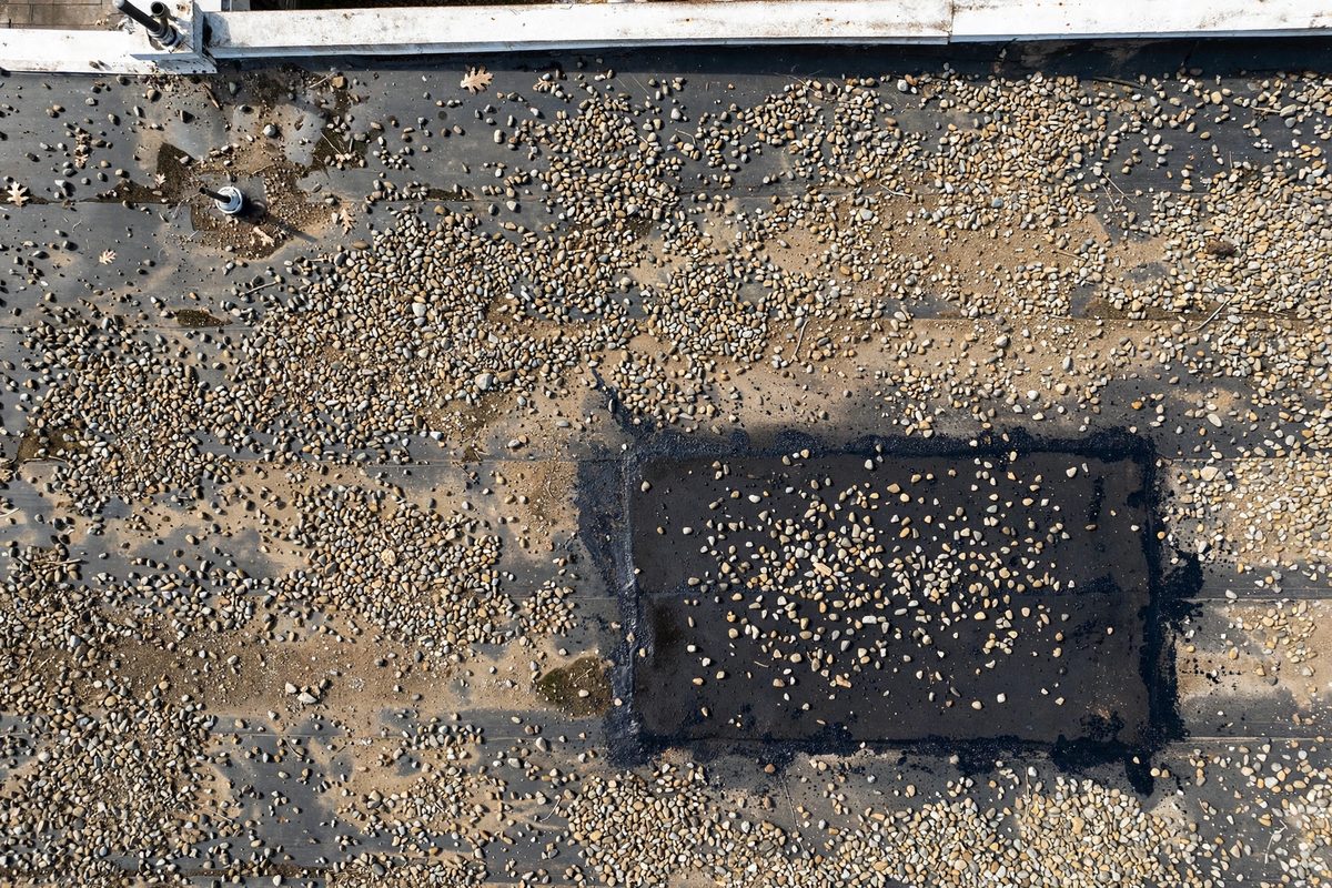 Built-up tar and gravel roof with a fresh patch from commercial roofing repair